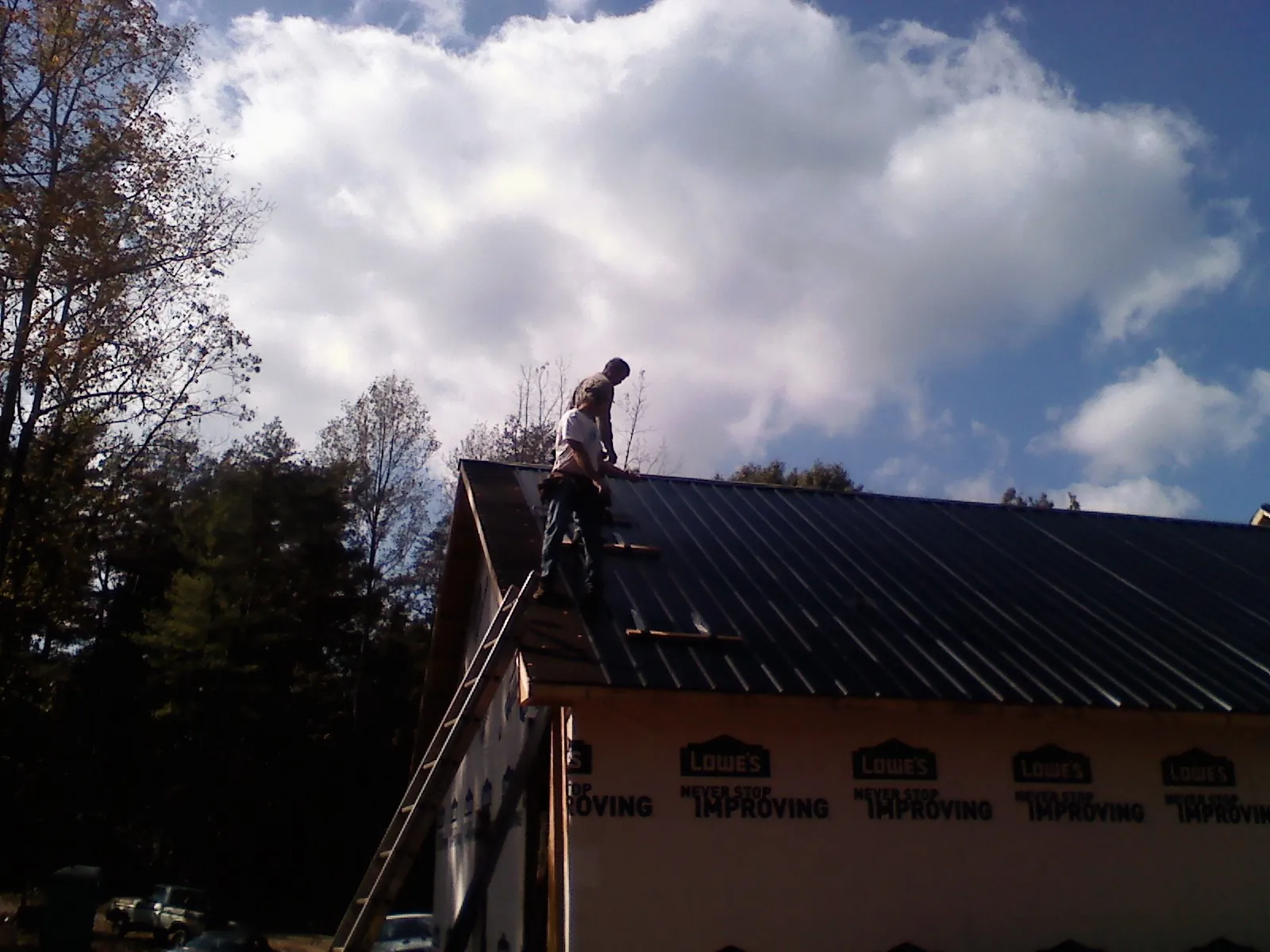 Roofer fastening dark metal panels high against a cloudy sky, from a Roof Inspection job in Canton